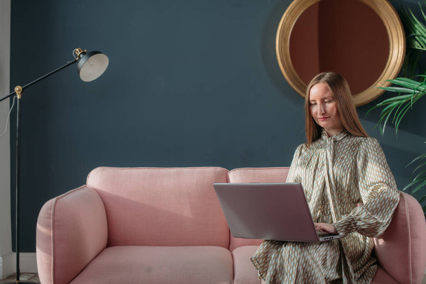 Zakelijke vrouw portret in modern kantoorinterieur met laptop. Stijlvol lachend jong meisje in een zakelijke jurk met een laptop op de bank. Vrouw in het bedrijfsleven, portret van een zakenvrouw. - Foto, afbeelding