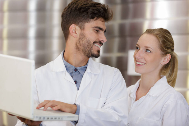 young man and woman wearing labcoats looking at laptop - Foto, imagen