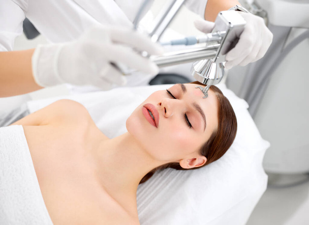 Profesjonalny kosmetolog wykorzystujący sprzęt laserowy do pielęgnacji skóry na twarzy klientki w nowoczesnej klinice kosmetycznej - Zdjęcie, obraz