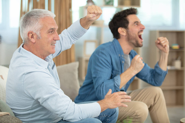excited man and father on couch watching football game - Фото, изображение