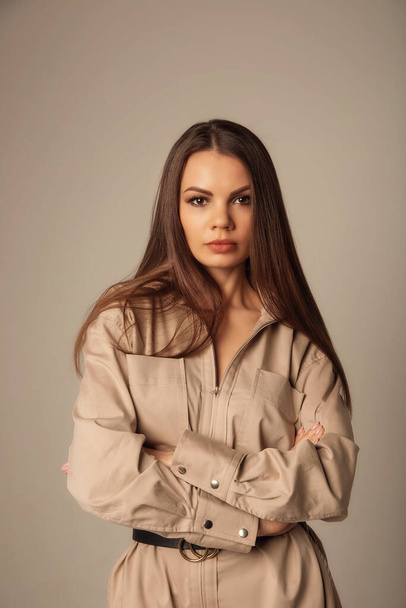 Portrait of young caucasian brunette woman in a beige blouse posing and looking at the camera over beige background - Foto, Imagen
