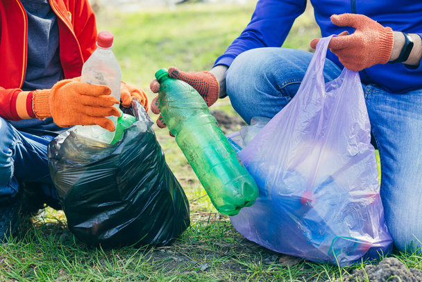 close up of volunteer man and son collecting garbage in park and forest. Ecology concept, hands of two people put a plastic bottle in a garbage bag - Фото, изображение