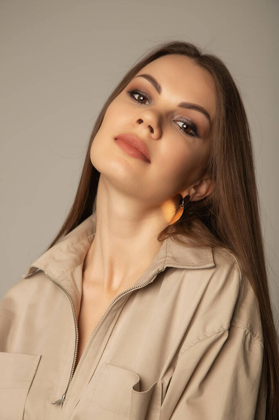 Portrait of young caucasian brunette woman in a beige blouse posing and looking at the camera over beige background - Valokuva, kuva