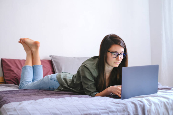 Young woman freelancer laying in bed and working with laptop. Remote job. - Fotografie, Obrázek
