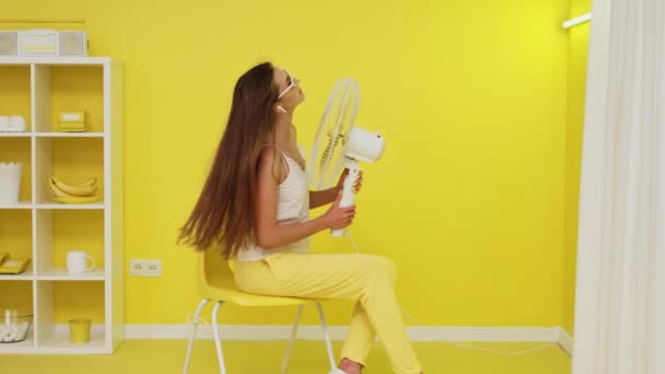 Mujer sexy con ventilador eléctrico está posando en la silla - Metraje, vídeo