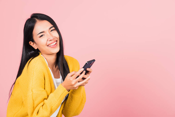 Happy Asian portrait beautiful cute young woman excited laughing holding mobile phone, studio shot isolated on pink background, female using funny smartphone making winner gesture - Φωτογραφία, εικόνα