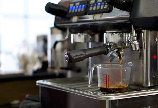 Μηχανή Espresso ρίχνει καφέ στο κύπελλο μέτρησης. Κλείσε. - Φωτογραφία, εικόνα
