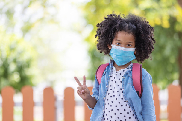 Child in face mask going at reopen school after covid-19 quarantine and lockdown. It is new normal for protection and prevention while outbreak of coronavirus or flu. Kids back to school concept. - Photo, Image