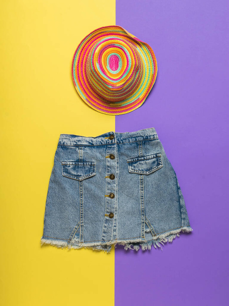 Multi-colored hat and denim skirt on a yellow and purple background. Summer denim clothing. - Photo, Image