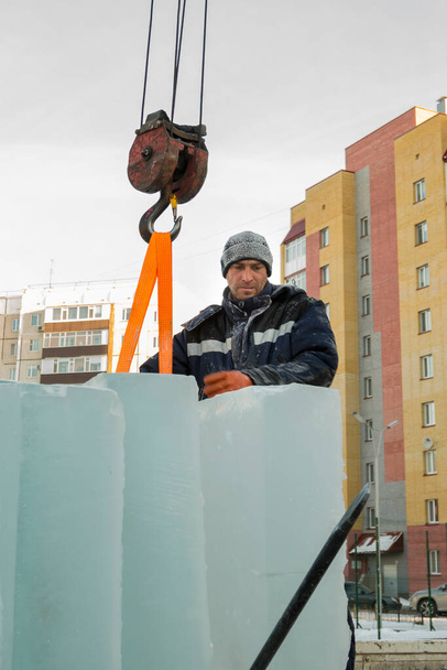 Retrato de um trabalhador em uma jaqueta azul com um capuz no gancho de um guindaste de caminhão - Foto, Imagem