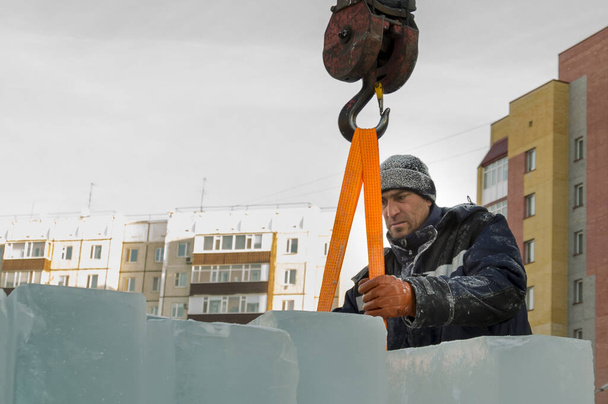 Retrato de un trabajador en una chaqueta azul con una capucha en el gancho de una grúa de camión - Foto, Imagen