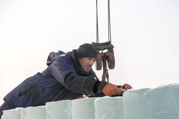 Portrait of a worker in a blue jacket with a hood at the hook of a truck crane - Photo, Image