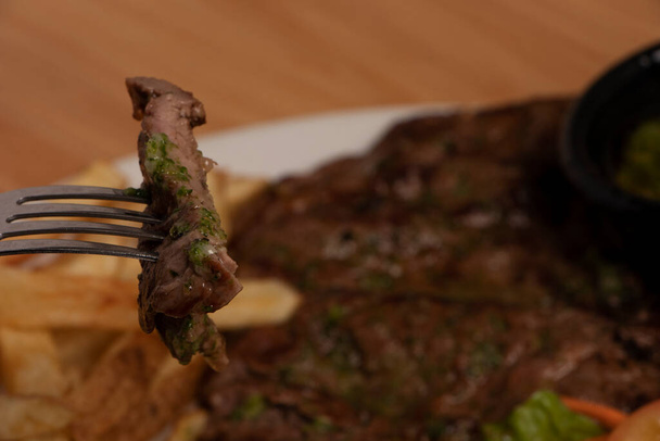Tenedor en primer plano con un trozo de carne y en el fondo de la foto el resto del plato - Foto, Imagen