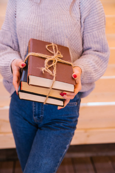A young woman stands and holds a stack of books in her hands. Books tied with string. The girl is a student, preparing for college or an exam. - Foto, Imagen