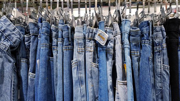 Monet farkut tai siniset housut roikkuu ruostumattomasta teräksestä ripustin myytävänä muotiliikkeessä. Kokoelma vaatteita ja denim käsite - Valokuva, kuva