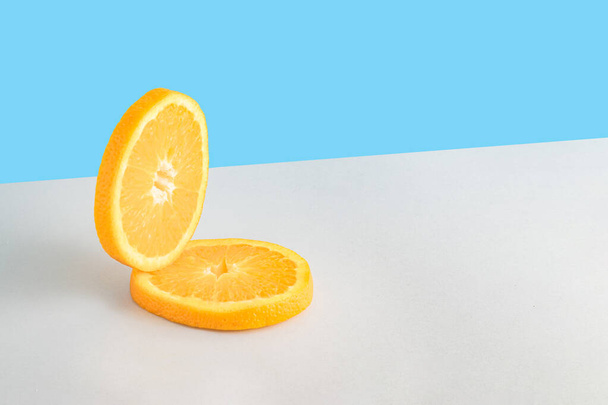 Творческая летняя композиция с двумя ломтиками свежего апельсина на синем и сером фоне. Минимальная свежая природа или концепция питания. - Фото, изображение