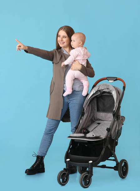 Woman with her cute baby and stroller on color background - Valokuva, kuva