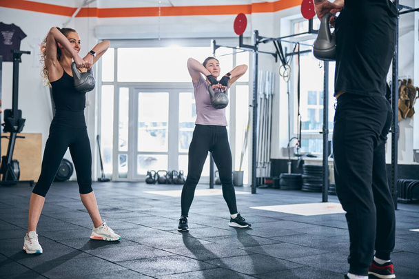 Attractive female athletes doing a strength training exercise with kettlebells - Photo, Image