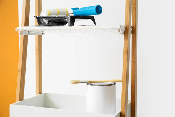Ladder with can of paint and tools near light wall, closeup - 写真・画像