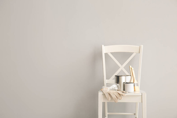 Chaise avec des boîtes de peinture et des outils près du mur léger - Photo, image