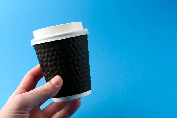 Hand houden koffie papier beker op blauwe achtergrond. - Foto, afbeelding