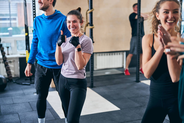 Merry athlete standing at the gym among her cheerful colleagues - Photo, Image