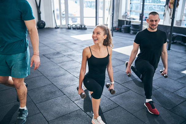 Smiling athletes doing the low lunge with dumbbells - Photo, Image