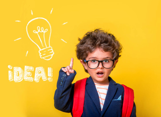 Back to school. School child in glasses isolated on yellow. Smart kid has idea with finger pointing up. Schoolchild with picture of light bulb. Innovation and creativity concept. Nerd pupil. - Zdjęcie, obraz