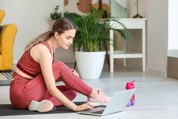 Urheilullinen nuori nainen, jolla on kannettava tietokone harjoittelemassa joogaa kotona lukituksen aikana - Valokuva, kuva