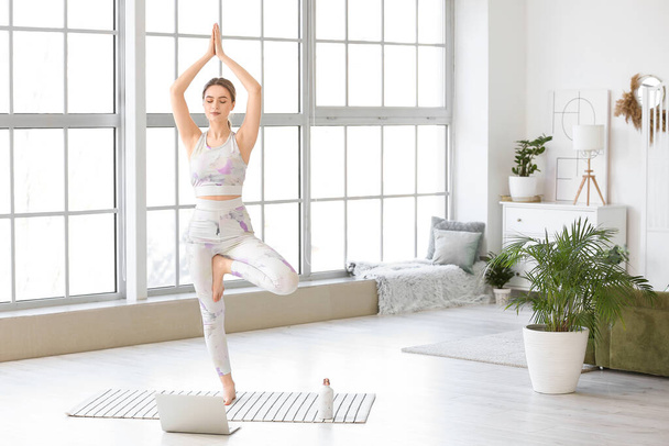 Giovane donna sportiva con laptop che pratica yoga a casa durante l'isolamento - Foto, immagini