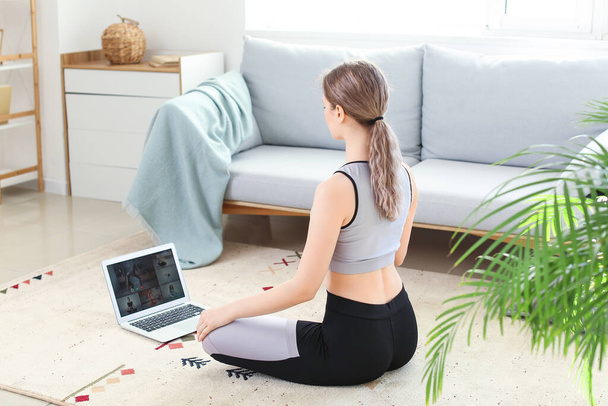 Mujer joven y deportiva con portátil practicando yoga en casa durante el encierro - Foto, imagen