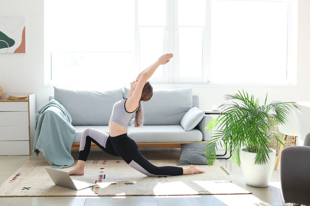 Mujer joven y deportiva con portátil practicando yoga en casa durante el encierro - Foto, Imagen