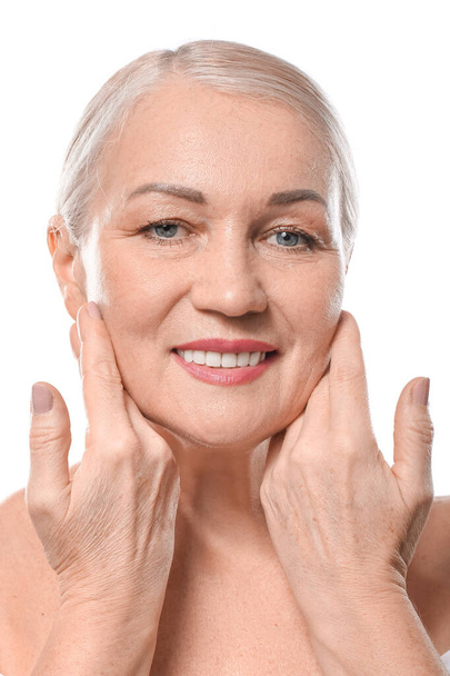 Mature woman giving herself face massage on white background - Foto, Imagem
