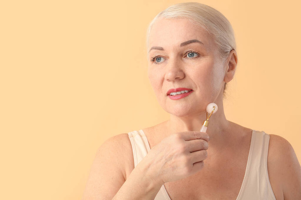 Mujer madura con herramienta de masaje facial sobre fondo de color - Foto, Imagen