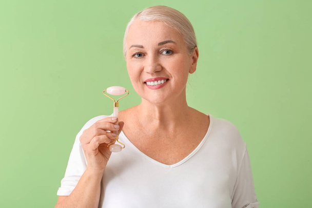 Femme mature avec outil de massage facial sur fond de couleur - Photo, image