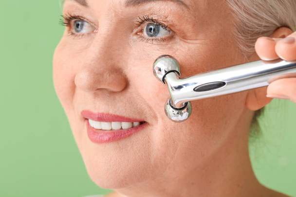 Mature woman with facial massage tool on color background - Foto, Imagen