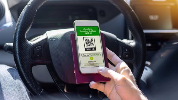 男性の手は車の中で国際予防接種証明書COVID-19 QRコードでパスポートとスマートフォンを保持 - 写真・画像