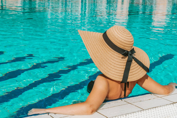 Jonge vrouwen zwembad. Gelukkig jong sexy meisje in bikini badpak, zonnebril en strohoed in blauw water. Vakantie op reis. Schoonheid, welzijn, levensstijl - Foto, afbeelding