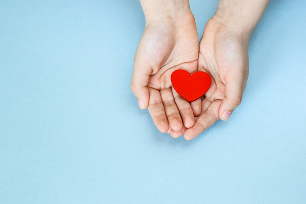 red heart in the hands of a child on a blue background, charity and care, blood donation - Photo, Image