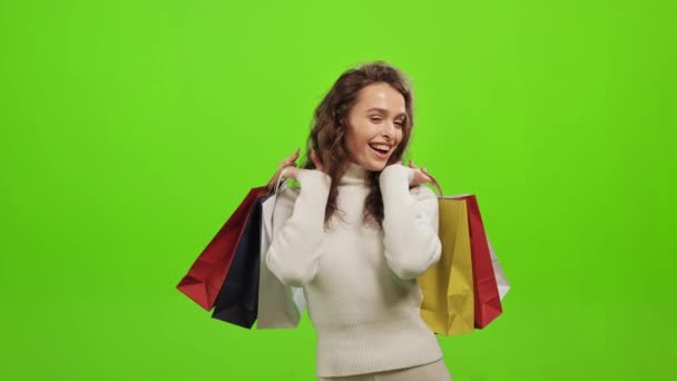 The woman is looking at the camera and smiling. She is raising up the shopping bags. Shes very happy. She is standing on a green background. Green screen. 4K - Felvétel, videó