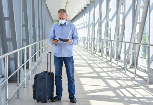 チケット、パスポート、空港またはショッピングモールでのスーツケース付きの医療マスクの男。コロナウイルス発生中の安全な旅行。ロックダウン、クォーランタン。安全なビジネス旅行 - 写真・画像