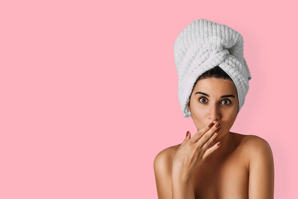 Beautiful woman with a towel on her head on a pink background. A young woman with beautiful eyes poses with a towel on her head on an isolated pink background. Bath and care concept. Spa. Copy space - Photo, Image
