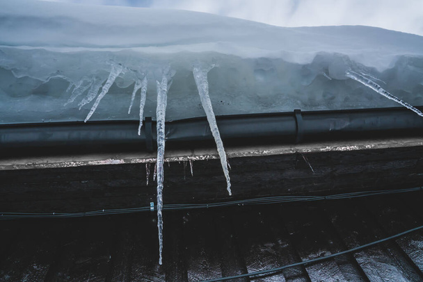 Ciclos pontiagudos longos de água congelada pendurada do lado de um telhado. Foto de alta qualidade - Foto, Imagem