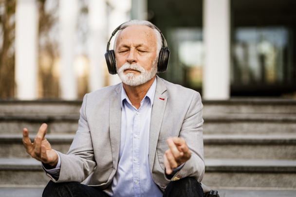 Счастливый старший бизнесмен медитирует после работы перед зданием компании. - Фото, изображение