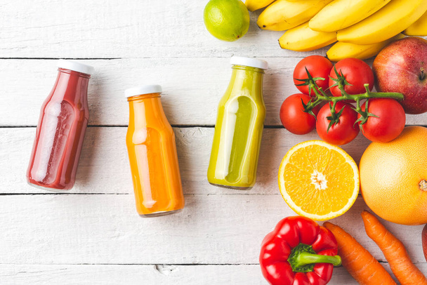 Overhead shot of fresh smoothies in bottles on white wooden table with fruits and vegetables - Foto, Imagen