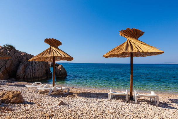 Veduta degli ombrelloni di paglia nella bellissima spiaggia di Oprna nella baia adriatica dell'isola di Krk, Croazia - Foto, immagini