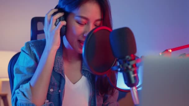 Mutlu Asyalı kız blogger synthesizer klavye çalıyor kulaklık takıyor ve ses mikseriyle birlikte geceleri oturma odasındaki stüdyoda müzik kaydediyor. Müzik içeriği oluşturucu, öğretici, yayın konsepti. - Video, Çekim