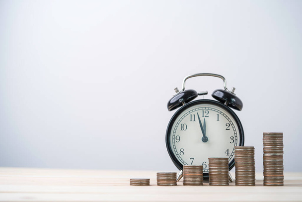 Monedas apiladas con despertador en mesa de madera, concepto de gestión de tiempo y dinero. - Foto, imagen