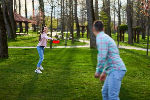 Casual dressed young couple playing freesbie in the park  - Zdjęcie, obraz