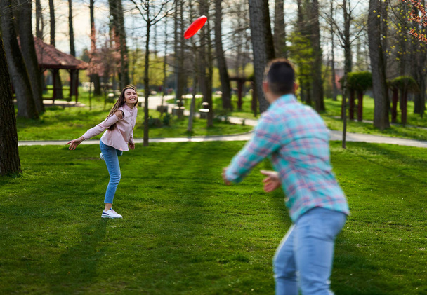 Casual dressed young couple playing freesbie in the park  - Фото, зображення